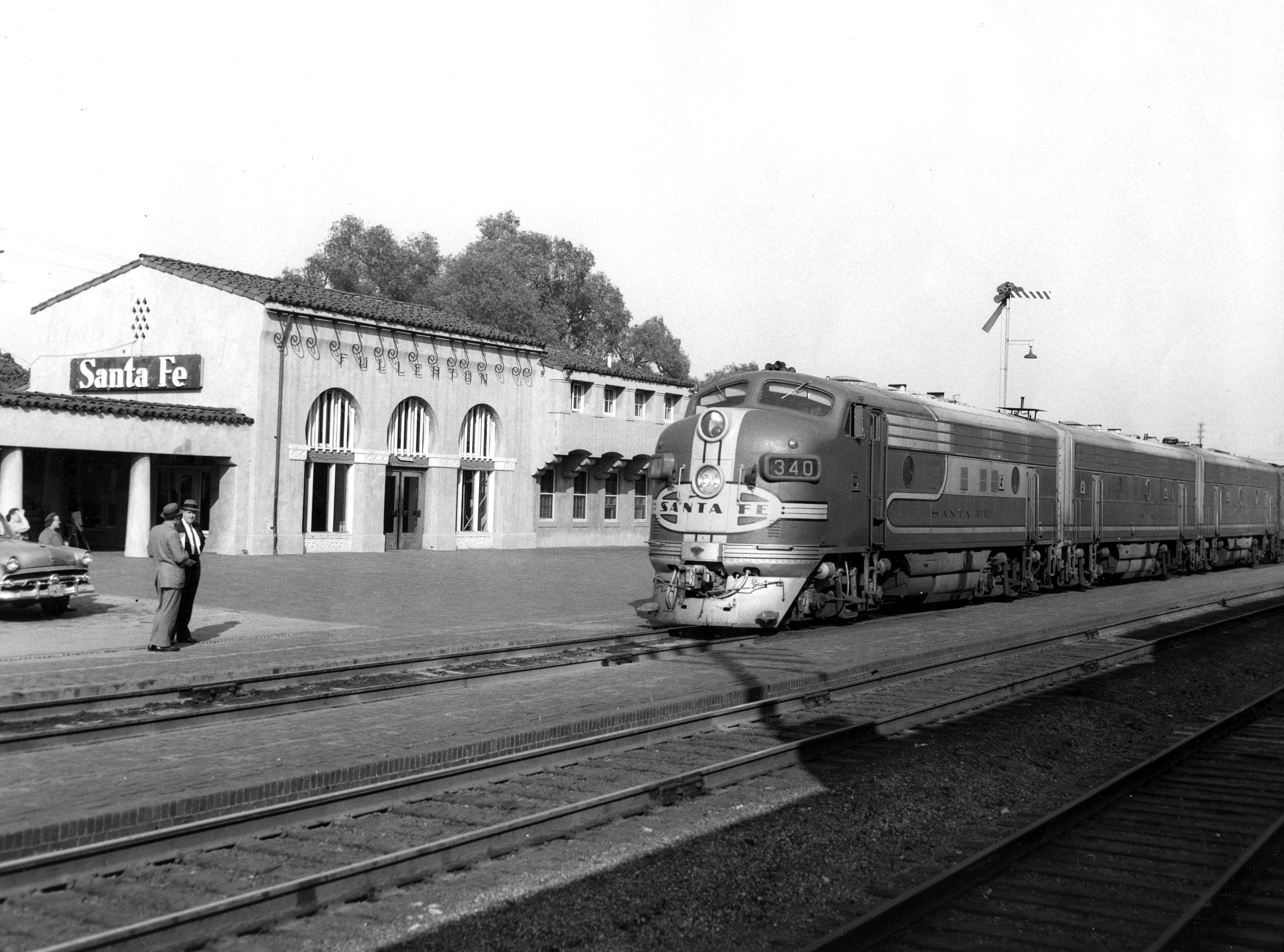 Passenger train pulling in to the Fullerton Santa Fe Depot in 1955, while two men wait on the platform.